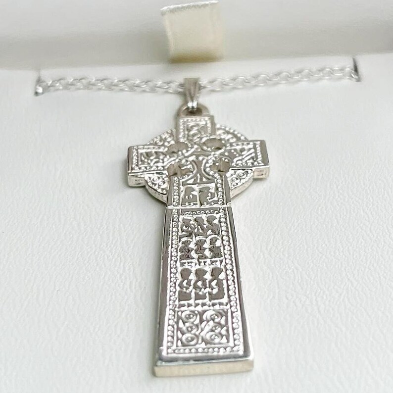 May include: A silver Celtic cross pendant necklace with intricate knotwork designs. The cross is detailed with a Celtic knot pattern and is suspended from a silver chain.