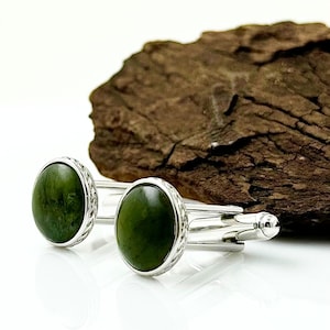 May include: A pair of silver cufflinks with green stone insets. The cufflinks have a decorative border around the stones.