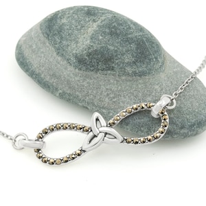 Infinity Necklace with Trinity Knot | Ireland Jewelry laying on a small grey stone in a white background