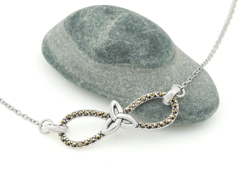 Infinity Necklace with Trinity Knot | Ireland Jewelry laying on a small grey stone in a white background