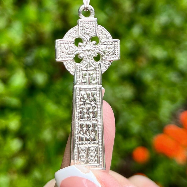 May include: Silver Celtic cross pendant with intricate knotwork design. The cross is detailed with a raised center and a textured border.