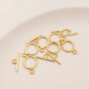 Puede incluir: Cierre de palanca de metal dorado con un anillo redondo y una barra recta. Estos cierres se utilizan para la fabricación de joyas y la artesanía.