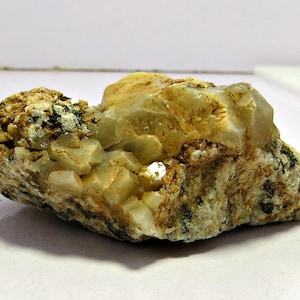 May include: A cluster of light brown and white crystals embedded in a rough, gray rock. The crystals have a translucent appearance and are arranged in a random pattern.