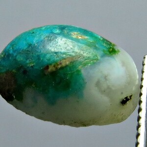 Op de afbeelding: Een close-up van een ovale cabochon edelsteen in groen en wit. De edelsteen heeft een gevlekt patroon van groen, wit en bruin.