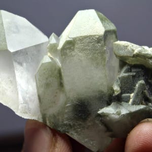 Puede incluir: Un grupo de cristales de cuarzo translúcidos, de color verde pálido. Los cristales tienen formas geométricas afiladas y tamaños variables, con una apariencia rugosa y texturizada. El color general es una mezcla de transparente y verde claro.