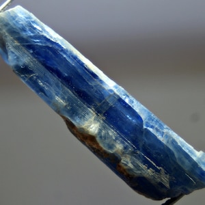 May include: A blue kyanite crystal with a striated surface. The crystal is translucent and has a light blue color.