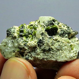May include: A small rock with green crystals embedded in it. The rock is surrounded by white crystals.