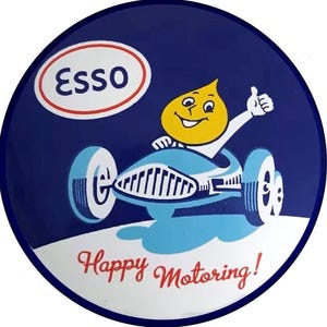 May include: A vintage Esso sign with a blue background and a white border. The sign features the Esso logo, a smiling yellow character in a blue race car, and the words "Happy Motoring!"