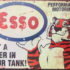 Puede incluir: Señal de metal vintage con un tigre de dibujos animados y el texto "Esso, Performance Motoring, Put a Tiger in Your Tank!"