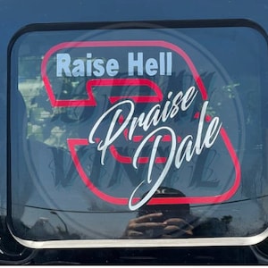 May include: Red and white vinyl sticker with the text "Raise Hell Praise Dale" in a stylized font.