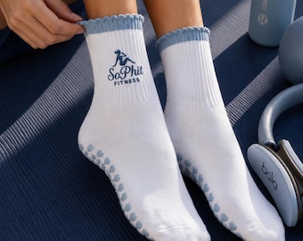 May include: A pair of white crew socks with a ribbed texture and a light blue ruffled cuff. The socks feature a dark blue graphic of a person exercising and the text "SoPhit FITNESS" printed on the side. The soles have light blue grip dots.