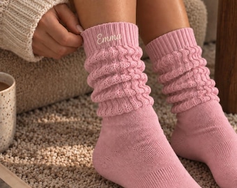 May include: A pair of light pink slouch socks featuring a ribbed knit texture and the name Emma embroidered in white script on the upper cuff. The socks are mid-calf length with a soft, knitted appearance and a solid color throughout the foot area.