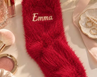 May include: A single red fuzzy sock with a textured, shaggy appearance. The name Emma is embroidered in a light-colored, cursive script across the upper portion of the sock. The material has a soft, long-pile finish throughout the entire surface.