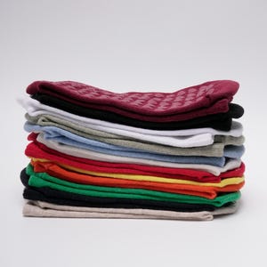 May include: A stack of folded socks in various solid colours including burgundy, black, white, grey, light blue, red, orange, yellow, green, and beige. The top burgundy pair features a textured pattern of small, raised grip dots on the fabric.