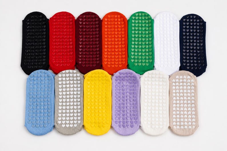 May include: A collection of thirteen low-cut ankle socks arranged in two rows, featuring a variety of solid colours including black, red, maroon, orange, green, white, navy, blue, grey, yellow, purple, cream, and beige with heart-shaped grips.