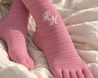 May include: A pair of pink toe socks featuring a ribbed cuff and individual compartments for each toe. The socks are crafted from a heathered knit fabric and display the white embroidered monogram letters RH on the outer side of the ankle area.