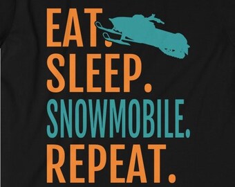 Puede incluir: Camiseta negra con texto naranja y azul que dice "Comer. Dormir. Moto de nieve. Repetir." Una silueta azul de una moto de nieve está sobre la palabra "Dormir."