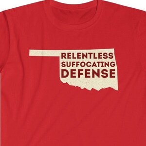 May include: Red t-shirt with a white outline of the state of Oklahoma and the text "Relentless Suffocating Defense".