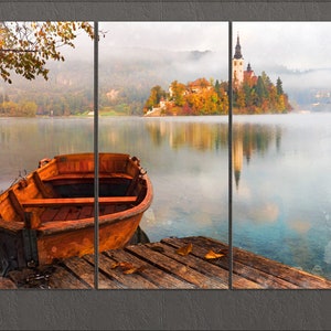 May include: A wooden rowboat sits on a wooden dock overlooking a lake with a small island in the distance. The island has a church with a tall steeple and trees with fall foliage. The lake is calm and reflects the sky and the island.