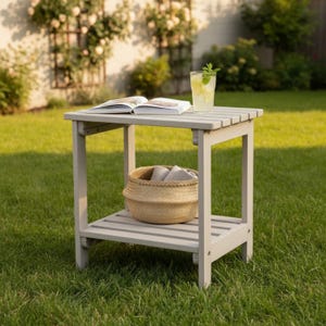 May include: A light gray outdoor side table with a slatted top and lower shelf. A woven basket with towels sits on the lower shelf. A book and a glass of lemonade with mint are on the table.