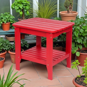 May include: A vibrant red outdoor side table with a slatted top and a lower shelf. The table is made of wood and has a rectangular shape. It is surrounded by potted plants, suggesting a garden setting.