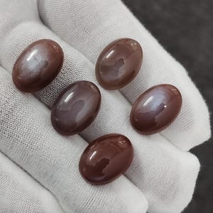 May include: Five oval-shaped, iridescent gemstone cabochons in shades of brown and purple. The stones have a smooth, polished finish and display a shimmering effect.