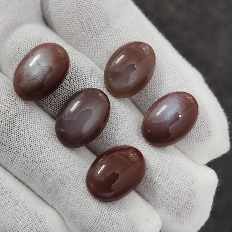 May include: Five oval-shaped, iridescent gemstone cabochons in shades of brown and purple. The stones have a smooth, polished finish and display a shimmering effect.