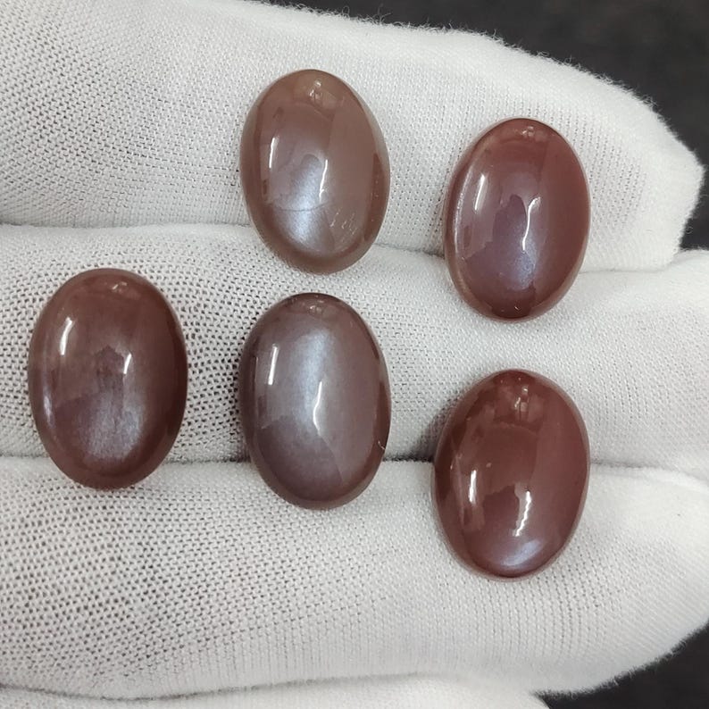 May include: Five oval-shaped, iridescent gemstone cabochons in shades of brown and grey. The stones have a smooth, polished surface and a subtle shimmer.