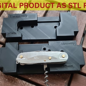 Könnte beinhalten: Schwarze 3D-gedruckte Montagekomponenten mit den Wörtern "Assembly" und "Disassembly". Ein silbernes Multitool befindet sich in den Komponenten. Der Text "DIGITAL PRODUCT AS STL FILE" steht in einem gelben Banner.