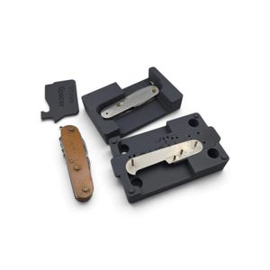 May include: A dark gray assembly jig for a 91mm pocket knife, featuring a spacer tool labeled 91mm Spacer, a metal base with three vertical pins, and two pocket knives with metallic and copper-colored handle scales.
