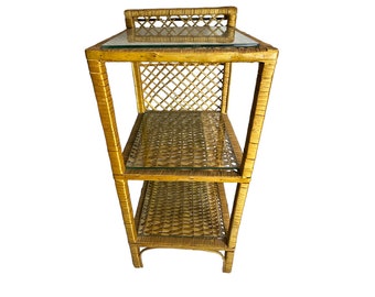 May include: A three-tiered wicker shelf unit with glass shelves. The shelf is made of natural woven wicker and has a light brown color.