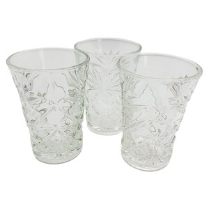 Puede incluir: Tres vasos de vidrio transparente con patrones texturizados en forma de diamante. Los vasos están vacíos y tienen un diseño simple y elegante. El fondo es blanco liso, resaltando la cristalería.