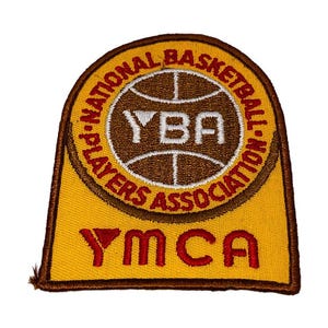 May include: A yellow and brown patch featuring the text "PLAYERS NATIONAL BASKETBALL ASSOCIATION" and "YBA" in white and brown. The word "YMCA" is in red at the bottom of the patch.