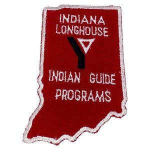 May include: A red patch shaped like Indiana, featuring white embroidered text: "INDIANA LONGHOUSE" and "INDIAN GUIDE PROGRAMS." A black and white "Y" logo is centered. The patch has a white stitched border.