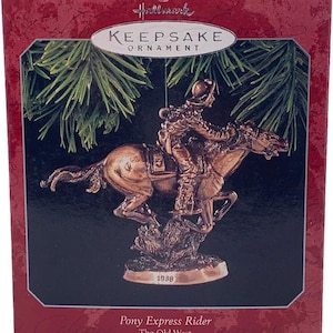 May include: A Hallmark Keepsake Ornament featuring a bronze-colored Pony Express Rider on horseback. The ornament is in a red box with the text "Pony Express Rider The Old West" and "New Collector's Series."