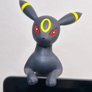 May include: A black and yellow 3D printed figurine of a Pokemon character, Umbreon, with red eyes. The figurine is perched on the edge of a black tablet.