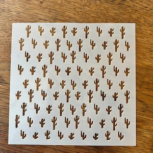 May include: White plastic stencil with a repeating pattern of small cactus silhouettes.