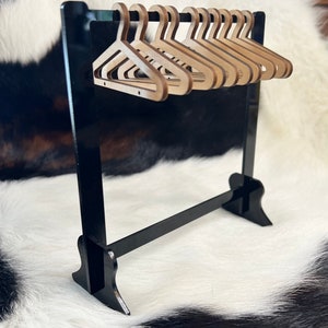 May include: A miniature black wooden clothes rack with a black metal bar and ten wooden hangers.