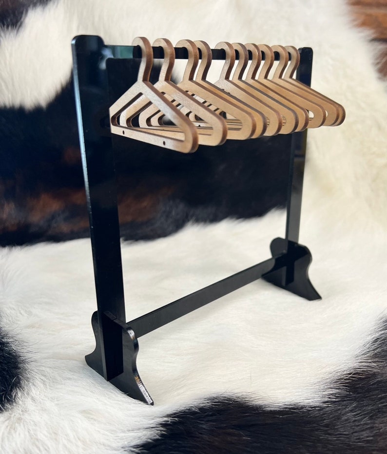 May include: A miniature black wooden clothes rack with a black metal bar and ten wooden hangers.