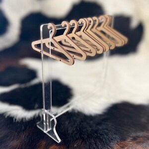 May include: A set of wooden hangers on a clear acrylic stand. The hangers are brown and have a simple design. The stand is made of clear acrylic and has a simple design.