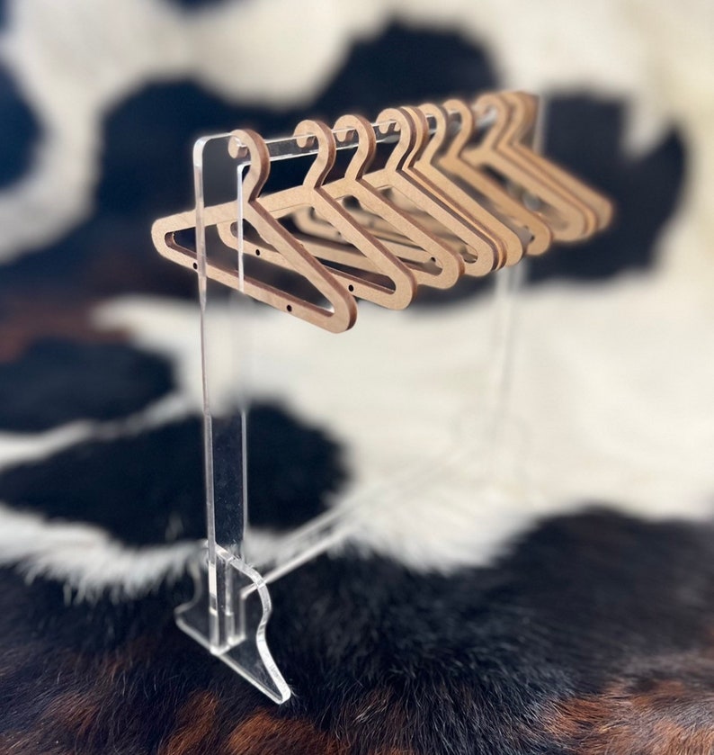 May include: A set of wooden hangers on a clear acrylic stand. The hangers are brown and have a simple design. The stand is made of clear acrylic and has a simple design.