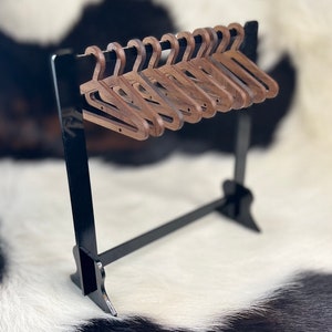 May include: A set of ten wooden hangers in a dark brown colour, hanging on a black metal rack. The hangers are all the same size and shape, and they are arranged in a neat row.