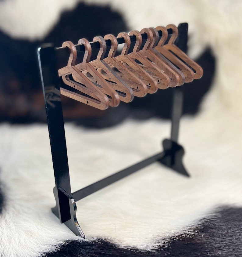 May include: A set of ten wooden hangers in a dark brown colour, hanging on a black metal rack. The hangers are all the same size and shape, and they are arranged in a neat row.