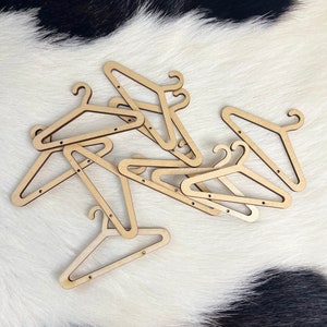 May include: A pile of wooden hangers, all in the same style, with a natural wood finish. The hangers are arranged in a random pattern on a white and black cowhide rug.