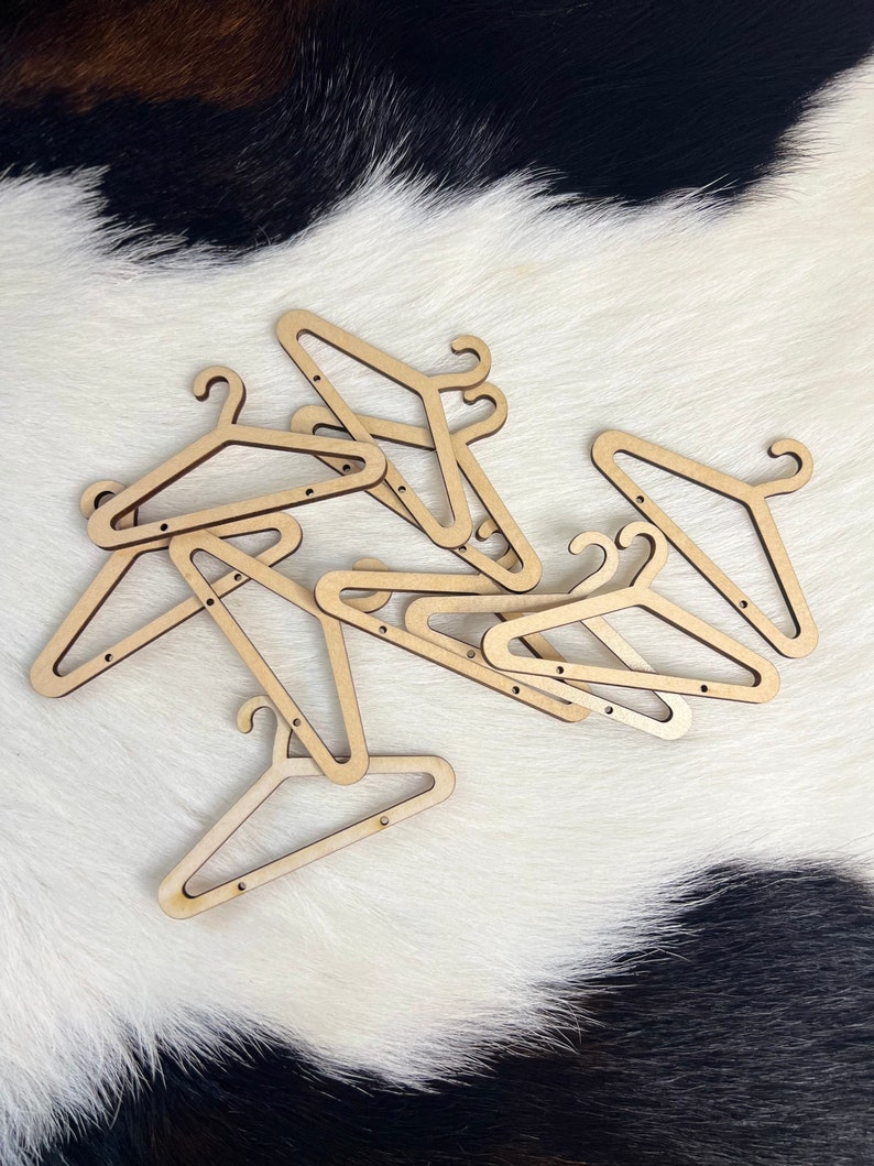 May include: A pile of wooden hangers, all in the same style, with a natural wood finish. The hangers are arranged in a random pattern on a white and black cowhide rug.