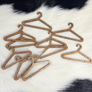 May include: A set of eight wooden hangers, all in a light brown colour, are scattered on a white and black cowhide rug. The hangers are all the same size and shape, with a simple design.