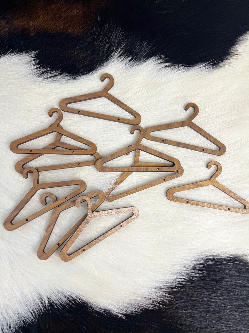 May include: A set of eight wooden hangers, all in a light brown colour, are scattered on a white and black cowhide rug. The hangers are all the same size and shape, with a simple design.
