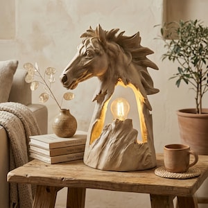 May include: A detailed beige horse head lamp, emitting a warm light. The lamp's design highlights the horse's mane and face. It's placed on a wooden table, alongside books and a small vase. The lamp's height is approximately 30 cm.
