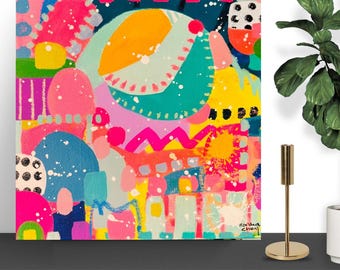 May include: Abstract art print with a vibrant mix of colors including pink, yellow, blue, and green. The artwork features organic shapes and splattered paint effects. The artist's signature is in the lower right corner. A gold candle holder is in the foreground.