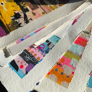 May include: A stack of white paper with colorful abstract designs and patterns. The paper has a textured surface and is slightly rough around the edges.